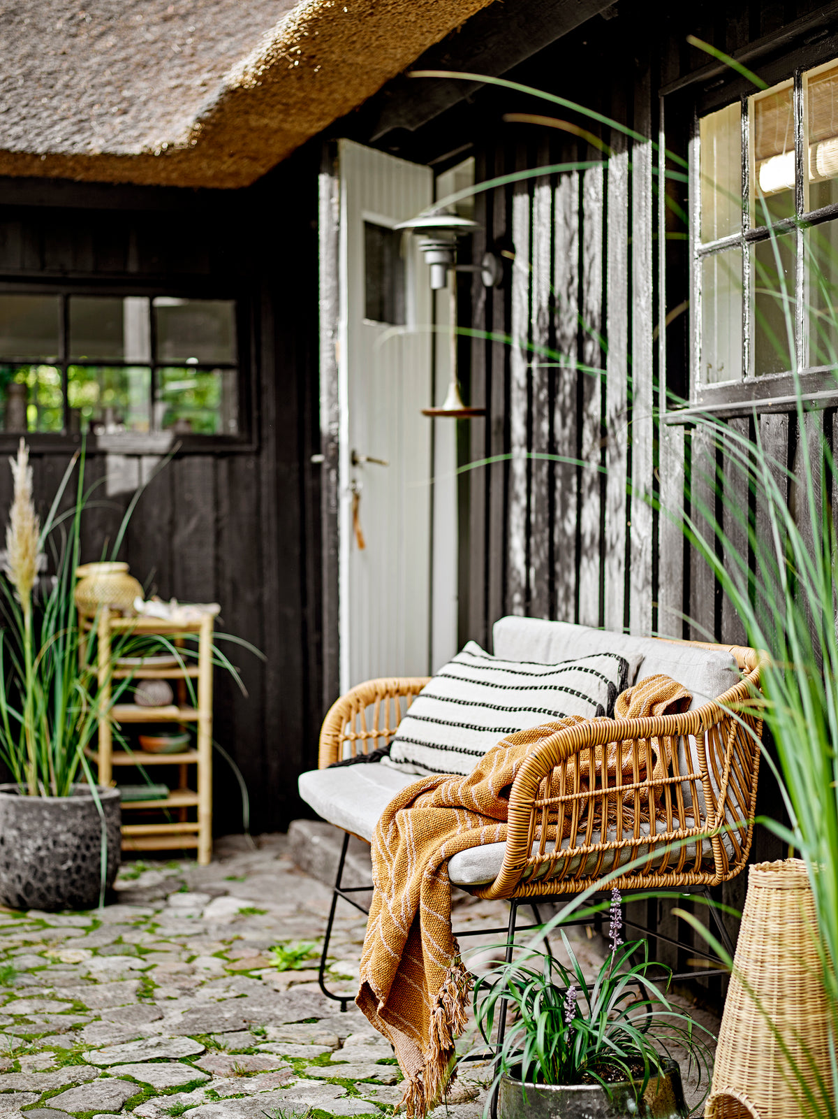 brown ginna throw draped over wicker outdoor bench creating warm scandi atmosphere
