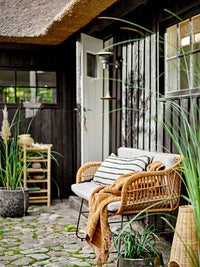 brown ginna throw draped over wicker outdoor bench creating warm scandi atmosphere
