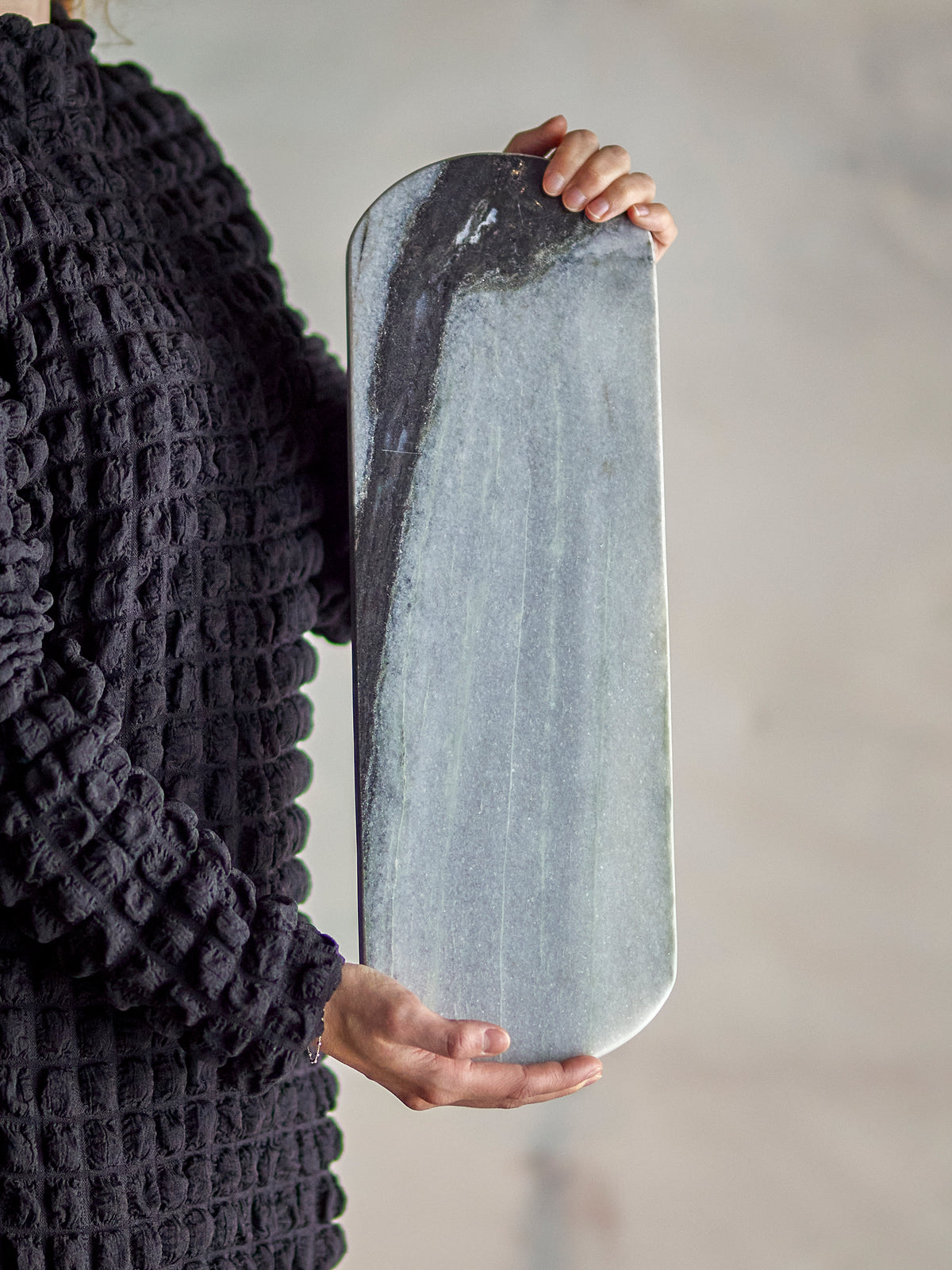 person holding long grey marble cutting board by bloomingville to show size and veining
