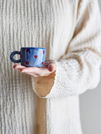 person holding tiny blue nini cup with hand-painted red hearts