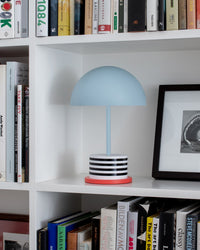 portable LED lamp with blue dome shade and striped base styled on a white bookshelf
