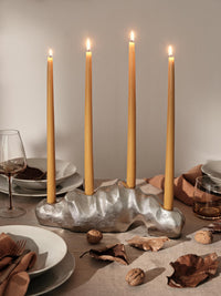 Golden yellow glossy taper candles lit in a silver sculptural holder on a set dining table