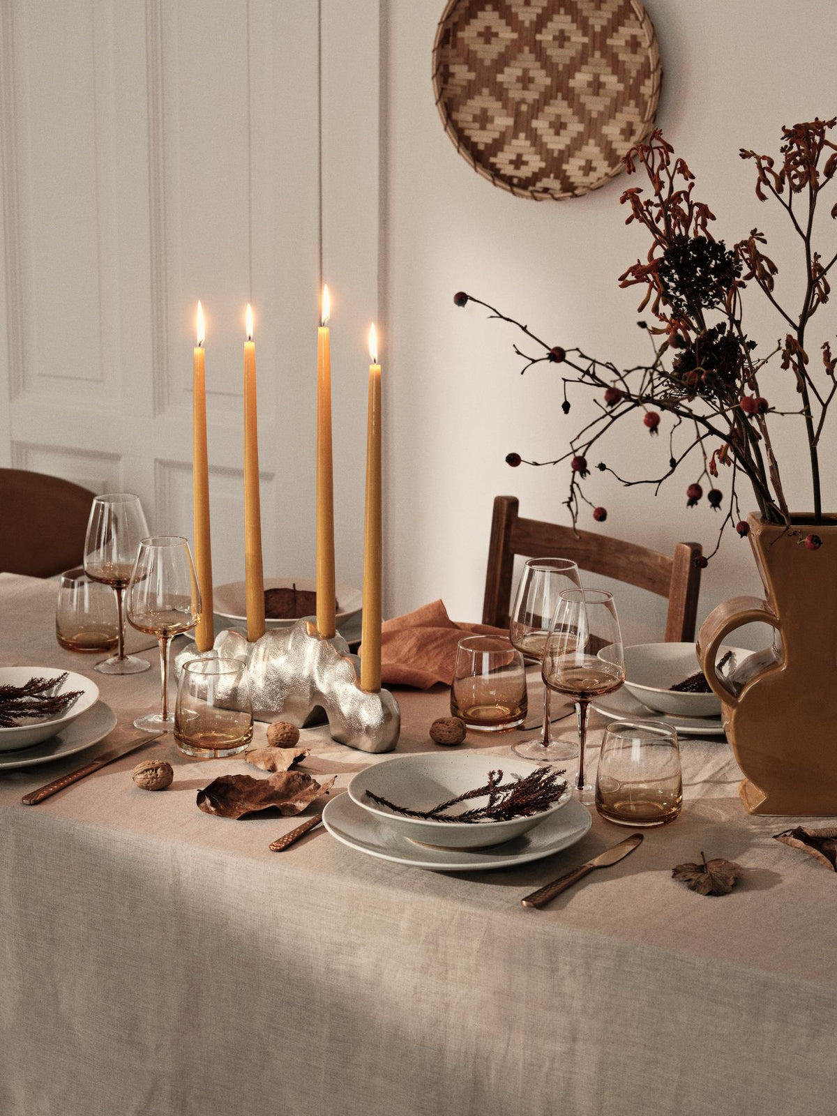 Golden yellow taper candles on a dining table dressed with dried branches and stoneware