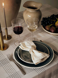 Brass Maro candle holders with tall taupe tapers on a dining table set with wine glasses