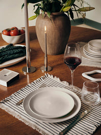 Silver Maro candle holders with lit taupe tapers on a wooden dining table with striped placemats