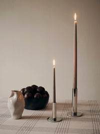 Small and large silver Maro candle holders with taupe tapers beside a ceramic jug and bowl