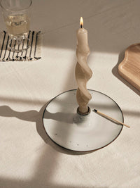 Lit cream twist candle in a Nordic Sand holder on a sunlit linen tablecloth