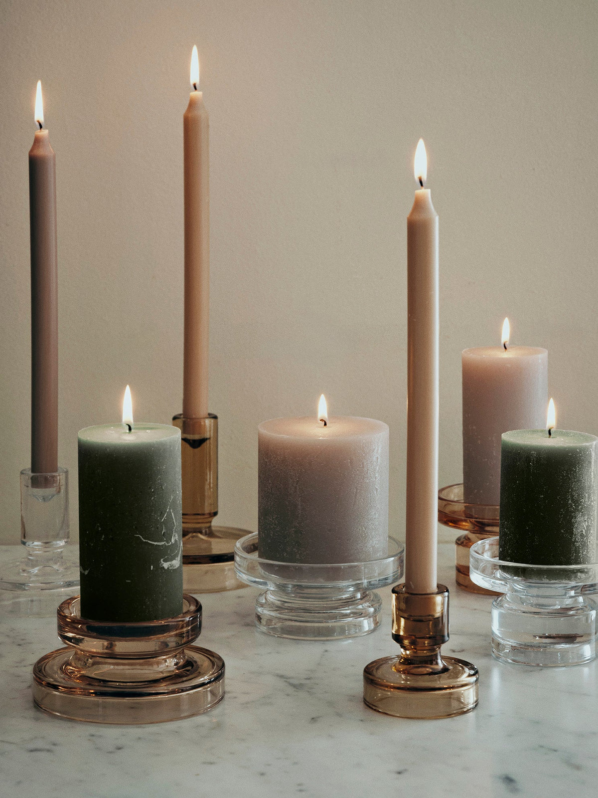 Group of Petra glass holders with green and grey pillar candles and tall tapers on a marble table