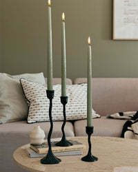 Sage green glossy taper candles in black sculptural holders beside a sofa