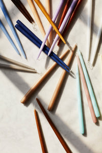 Smooth taper candles in a range of colours laid across a pale marble surface