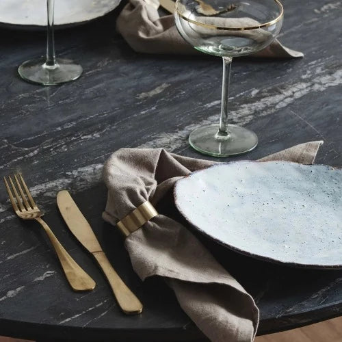 A black marble table set with plates, golden cutlery, and of course a napkin held with a golden napkin ring