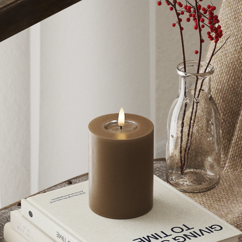 realistic large caramel LED candle glowing in a cosy winter home setting

