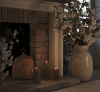 set of caramel LED pillar candles glowing warmly on a stone fireplace with glass lanterns
