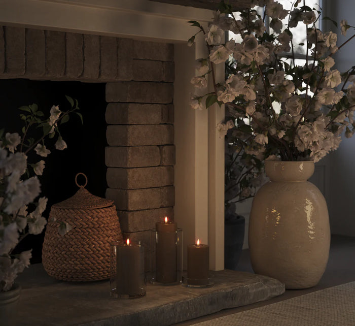 set of caramel LED pillar candles glowing warmly on a stone fireplace with glass lanterns
