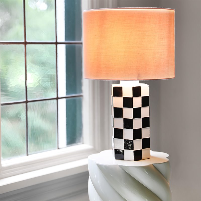 Black and white Check table lamp lit with a warm pink glow beside a window