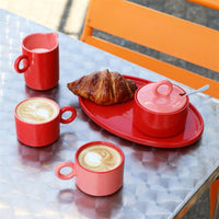 Red Chiquito sugar pot, milk jug and tray with cappuccinos and a croissant on a cafe table