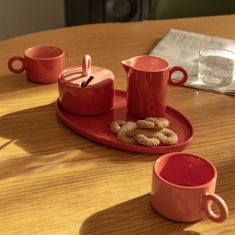 Red Chiquito tray with sugar pot, milk jug, biscuits and mugs on a sunny wooden table