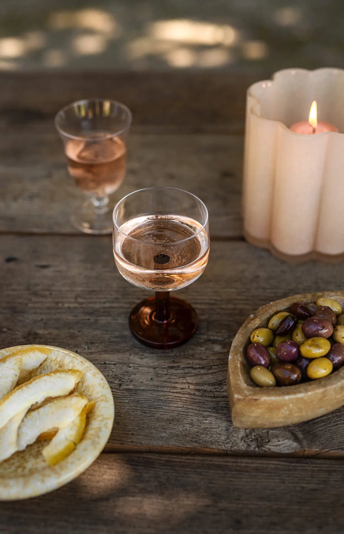 Lit Clara votive by Olsson & Jensen on an outdoor table with rosé glasses and snacks