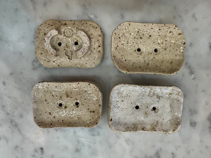 Four rectangular stone-like soap dishes with drainage holes on a marble surface