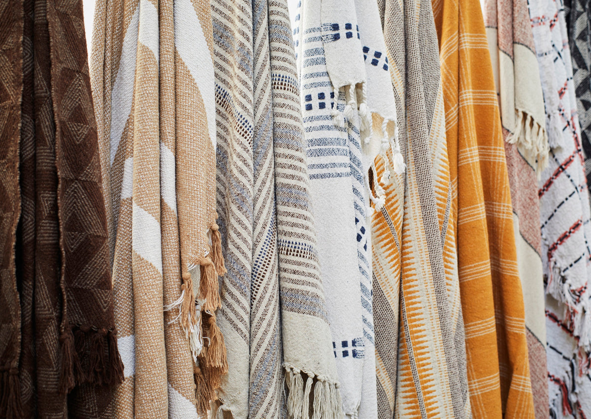 Close-up of hanging throws including warm honey and ecru striped recycled cotton design