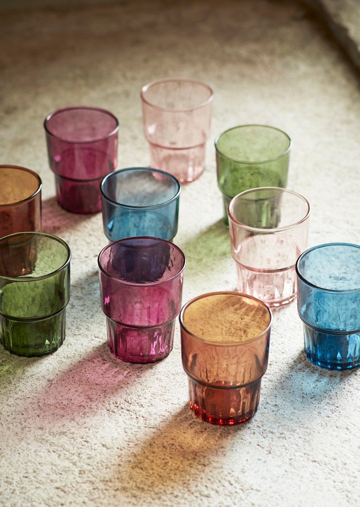 collection of colourful drinking glasses in natural light on stone surface
