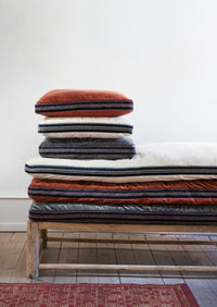 stack of cotton velvet mattresses in warm tones on wooden bench in Scandinavian interior