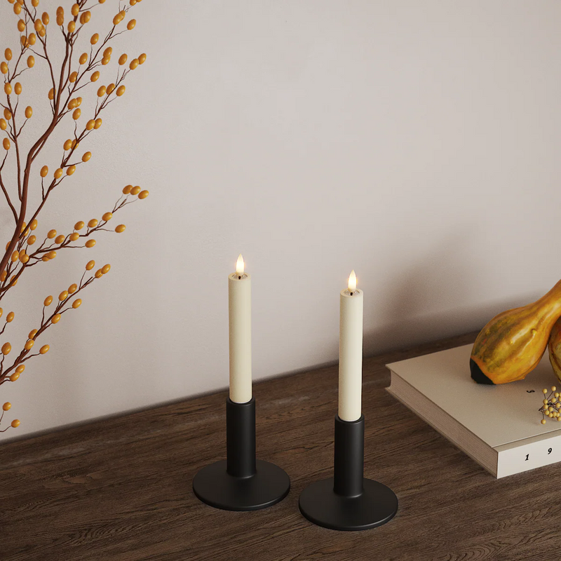 Pair of cream LED dinner candles on a wooden surface with autumnal decor for a warm, inviting glow.
