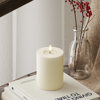 small cream LED pillar candle glowing softly in a neutral winter interior
