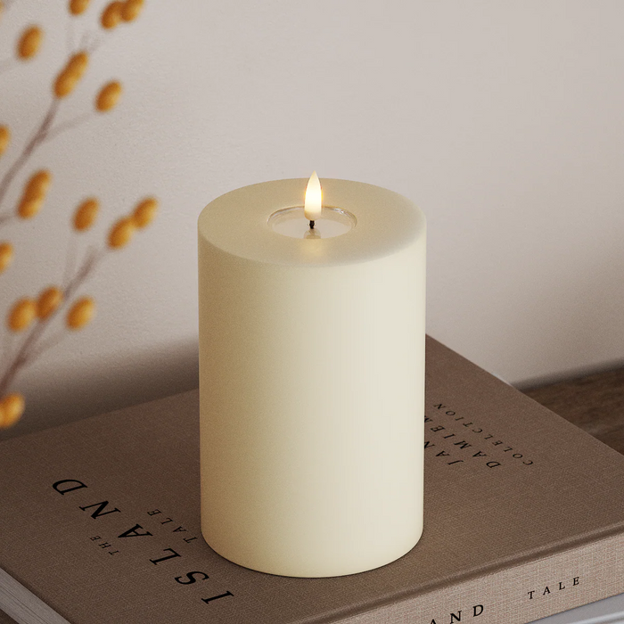 cream wax-coated LED pillar candle with warm flickering flame styled on books in a soft autumn interior
