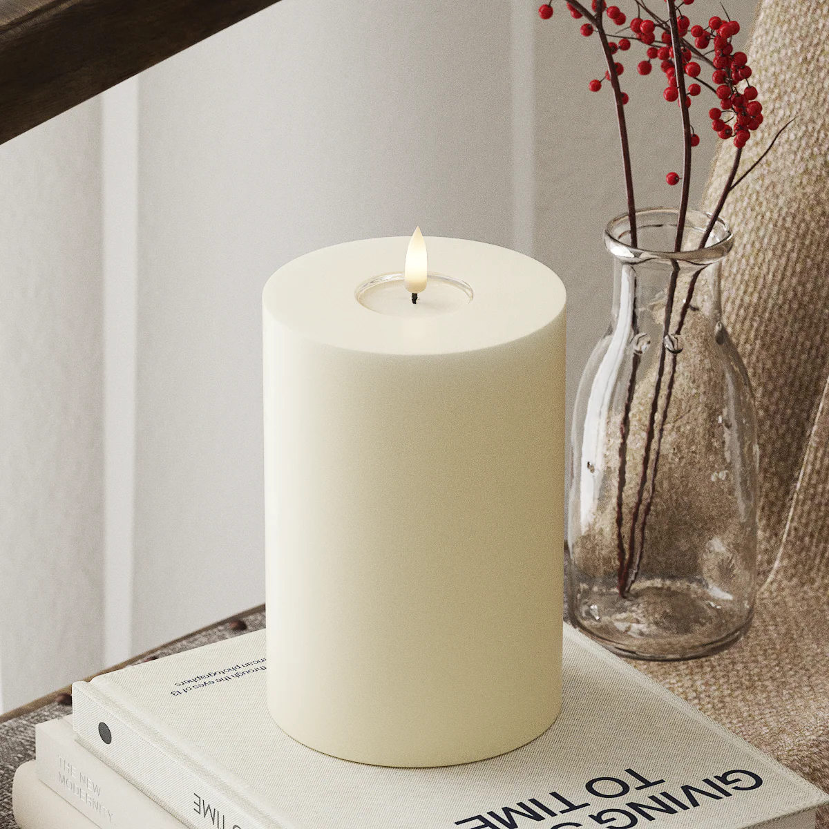 realistic cream LED candle glowing softly beside winter foliage in a calm neutral home

