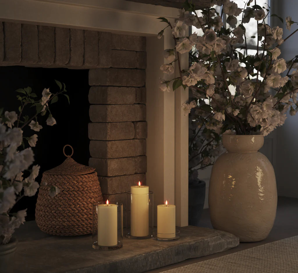 set of cream LED pillar candles glowing warmly in glass holders on a stone fireplace
