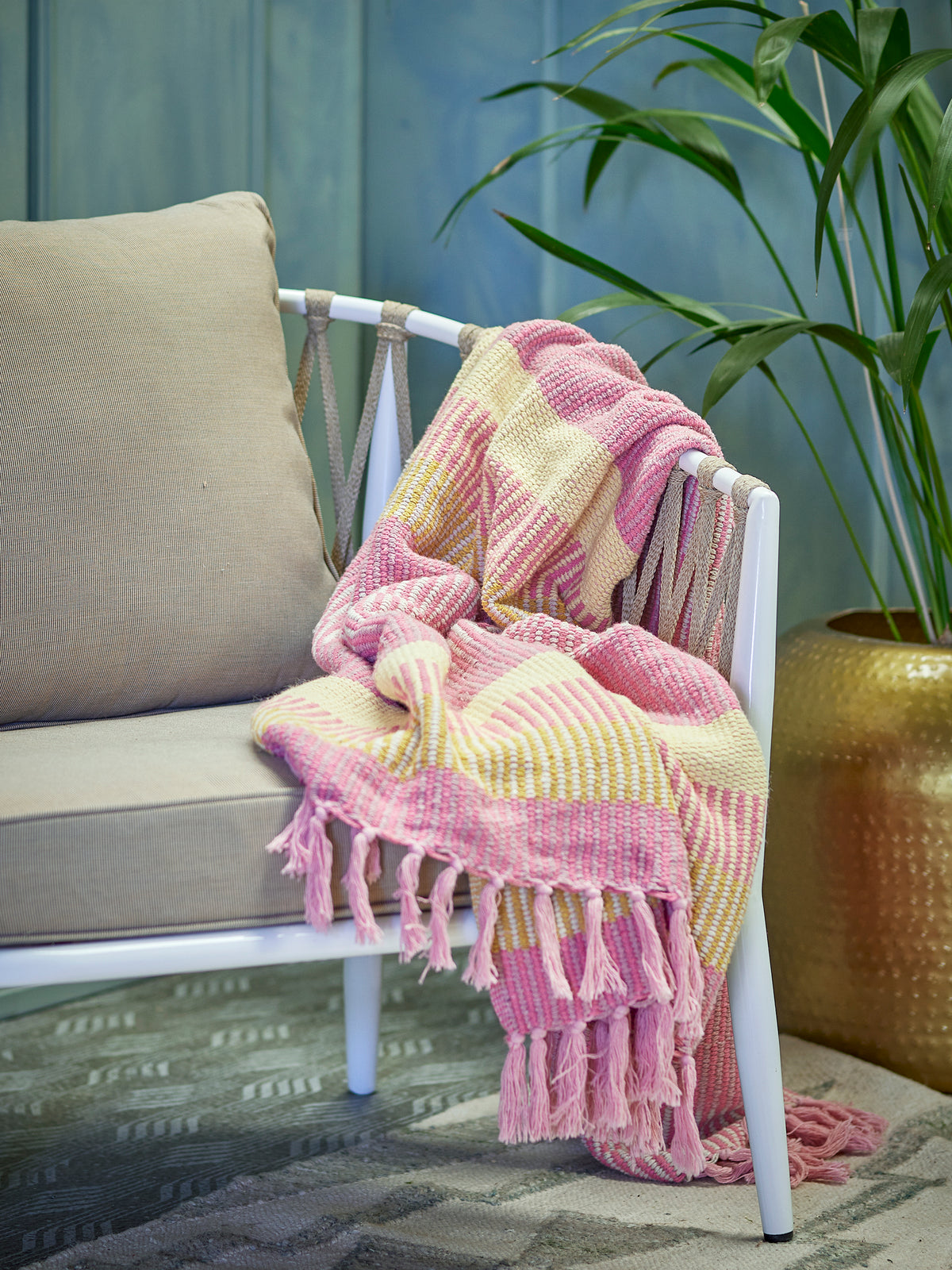pink and yellow striped recycled cotton throw draped over a neutral chair in a cosy styled space