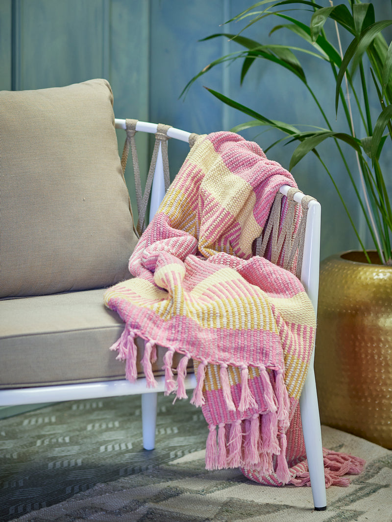 pink and yellow striped recycled cotton throw draped over a neutral chair in a cosy styled space