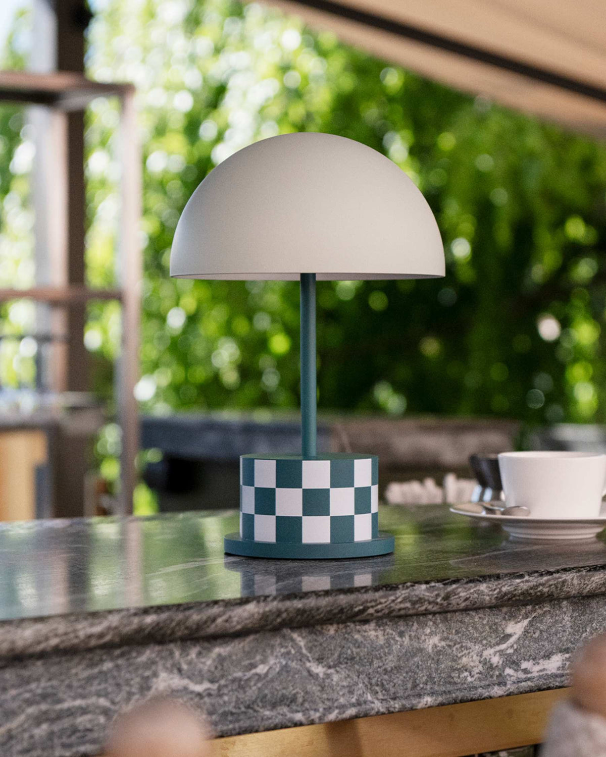 teal checkered portable lamp on outdoor countertop with greenery behind
