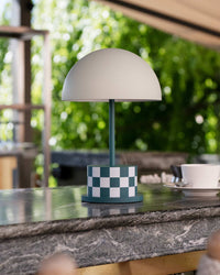 teal checkered portable lamp on outdoor countertop with greenery behind
