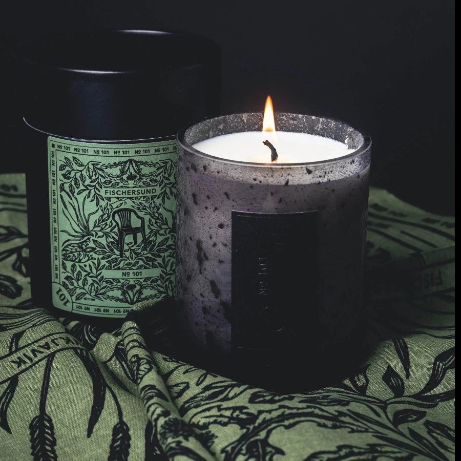 fischersund number 101 scented candle in its light grey reusable glass jar with dark speckles and gently flikering with a beautiful flame