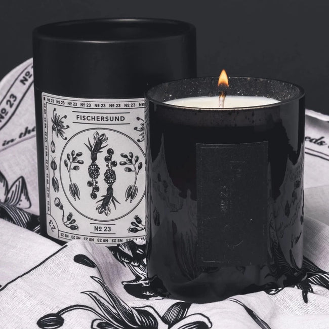 a lit black jar containing a fischersund 23 scented candle that is lit and stood on it's bandana
