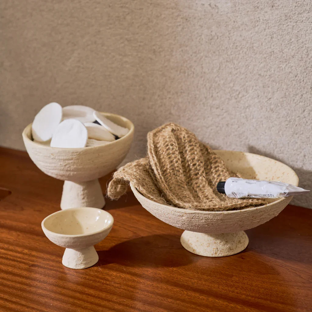 Flad and smaller footed bowls holding soaps and a washcloth on a wooden counter