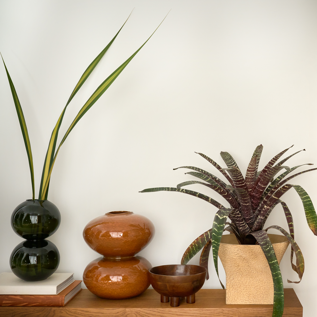 Foss vase styled on a low bench with plants and a dark green vase
