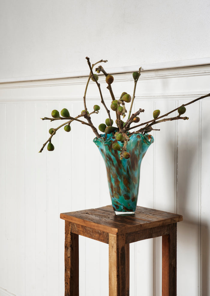 art deco inspired green and blue speckled glass vase styled on wooden stand
