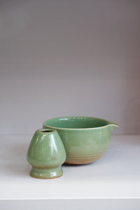 glossy green matcha bowl and whisk holder set on white shelf
