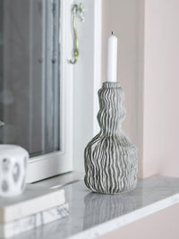Tall polyresin candle holder with wavy surface texture on marble windowsill