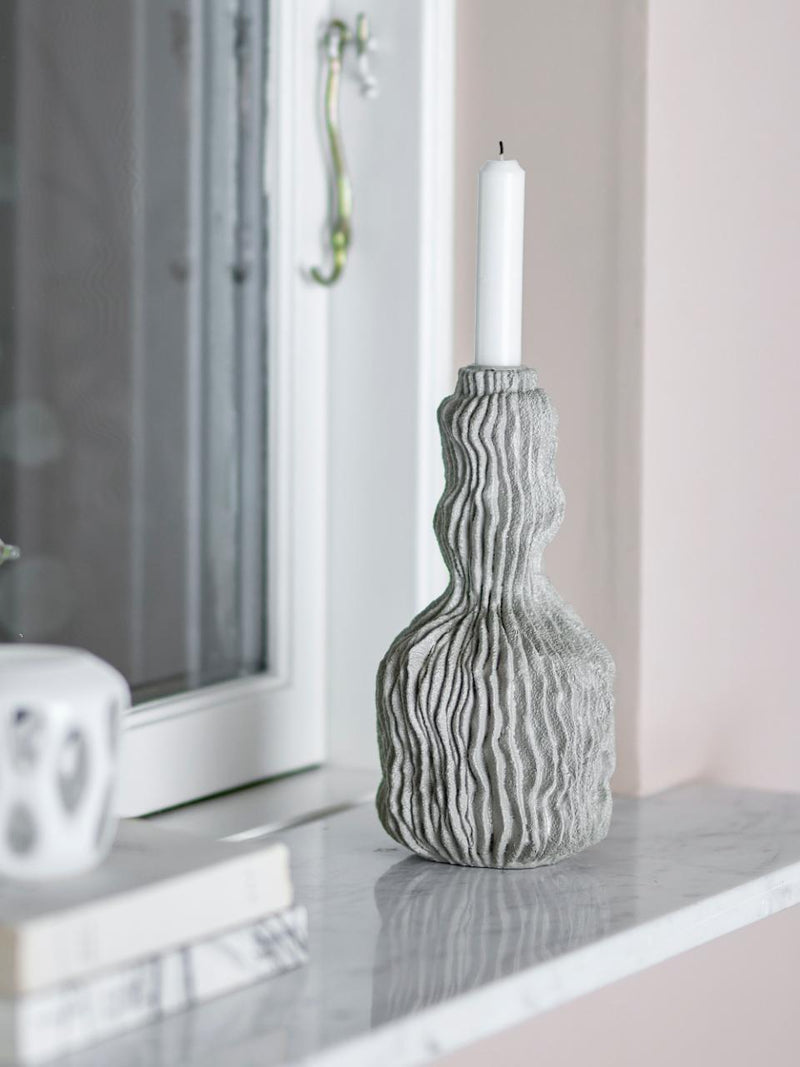 Tall polyresin candle holder with wavy surface texture on marble windowsill