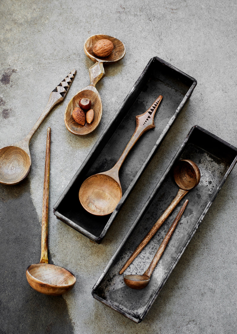 carved mango wood spoons and ladles arranged in metal trays on concrete surface
