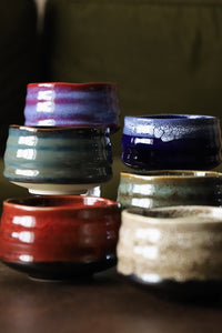 Red lava matcha bowl in front of a group of handmade matcha bowls in mixed glazes