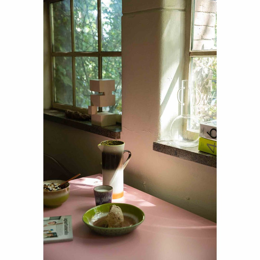 kitchen setting with a jug and plate oon a table and the white wooden abject on a windowsill in the background