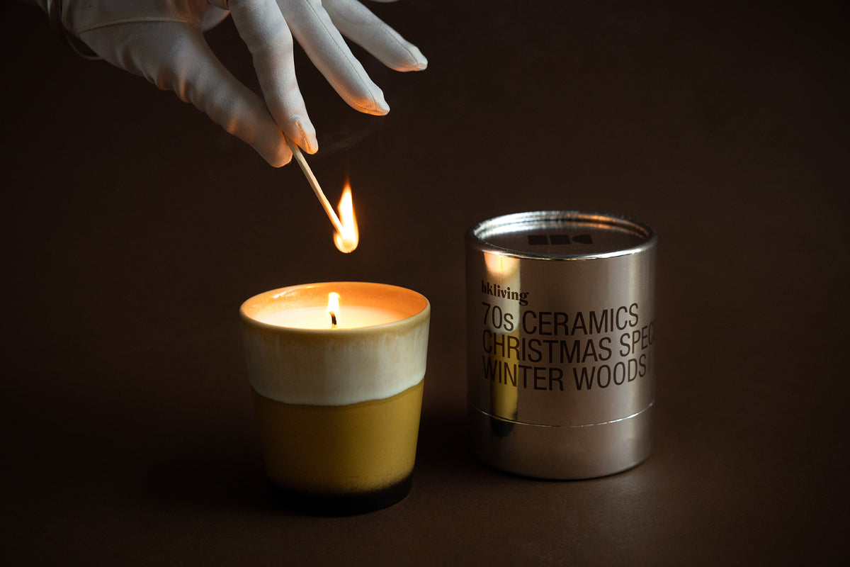 Close-up of HKLIVING Winter Woods candle flame beside metallic packaging – warm festive styling
