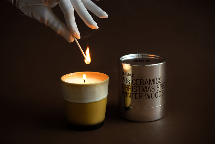 Close-up of HKLIVING Winter Woods candle flame beside metallic packaging – warm festive styling
