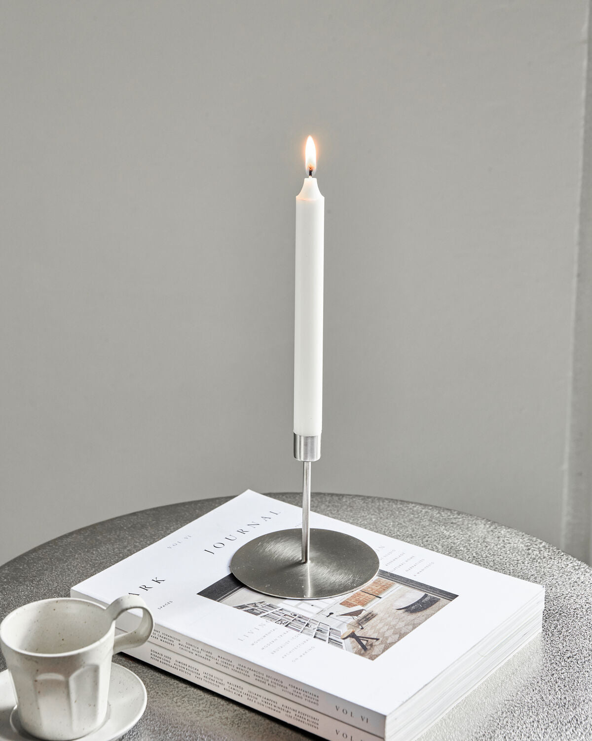 Medium House Doctor Anit silver candle holder with a lit candle on a stack of magazines