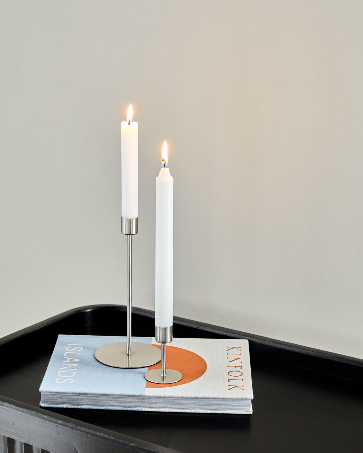 Short and Tall House Doctor Anit silver candle holders with lit candles on a black tray